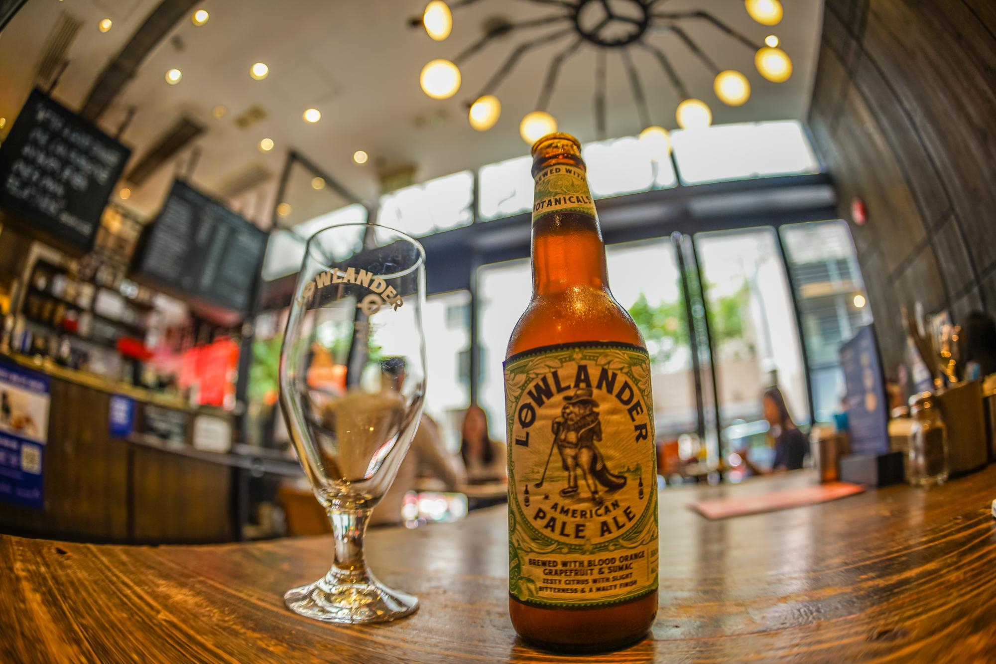 A Lowlander pale ale bottle and branded glass on a wooden pub bar